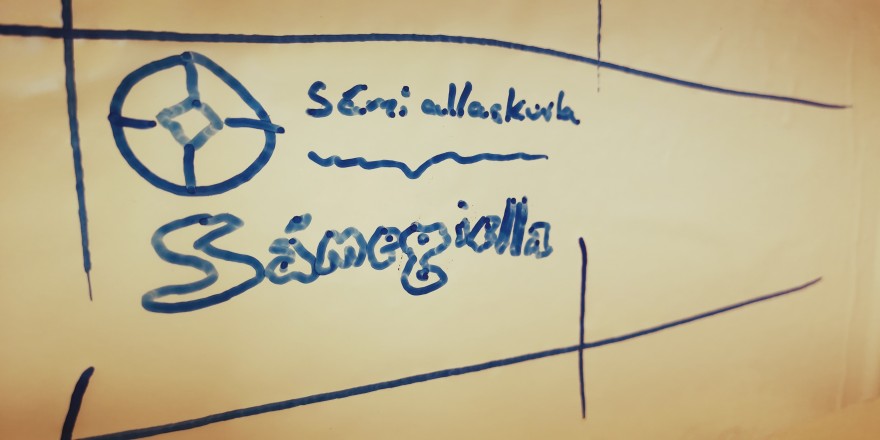 Giella Govva whiteboard tavvalis mas sárgojuvvon Sámi allaskuvla namma, logo ja sátni Sámegiella.