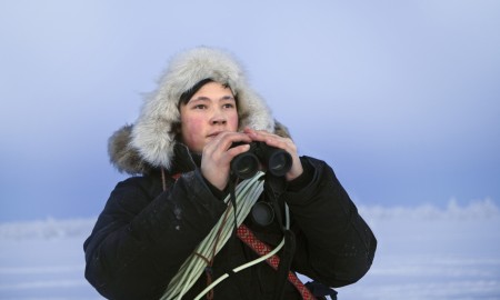 Bilde av en reingjeter med kikkert i hånden og lasso rundt skuldrene.